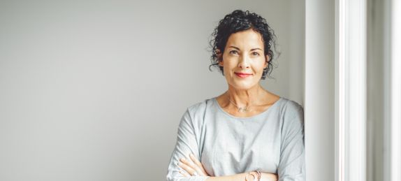 Frau lehnt lächelnd an einer Wand